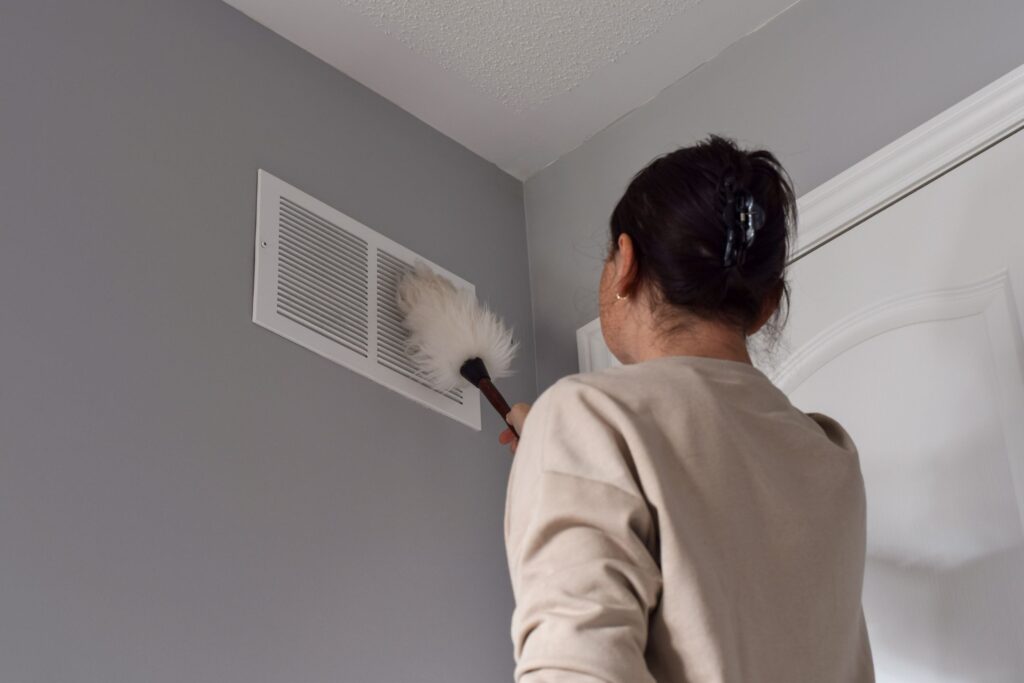 image of a woman cleaning an air duct with a feather duster