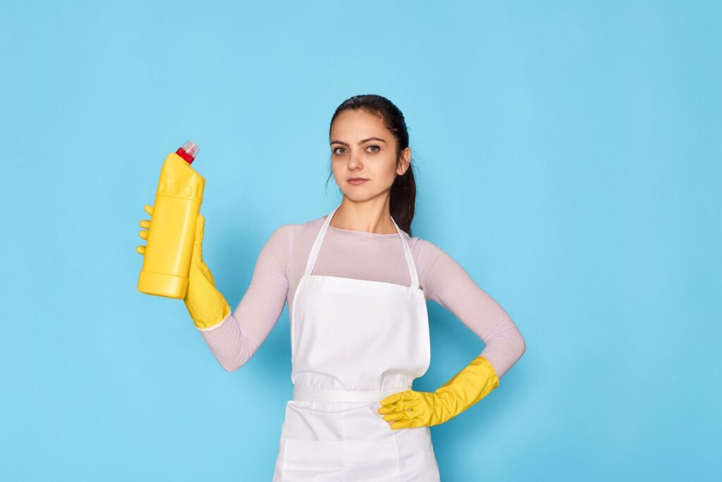 image of a woman holding a yellow container with cleaner in it, wearing a white apron and yellow gloves