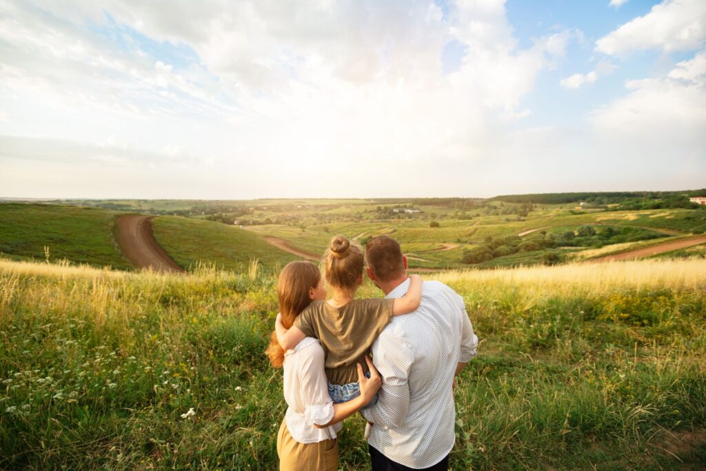 a family of three looking out over a field at a countryside scenery and small village or town